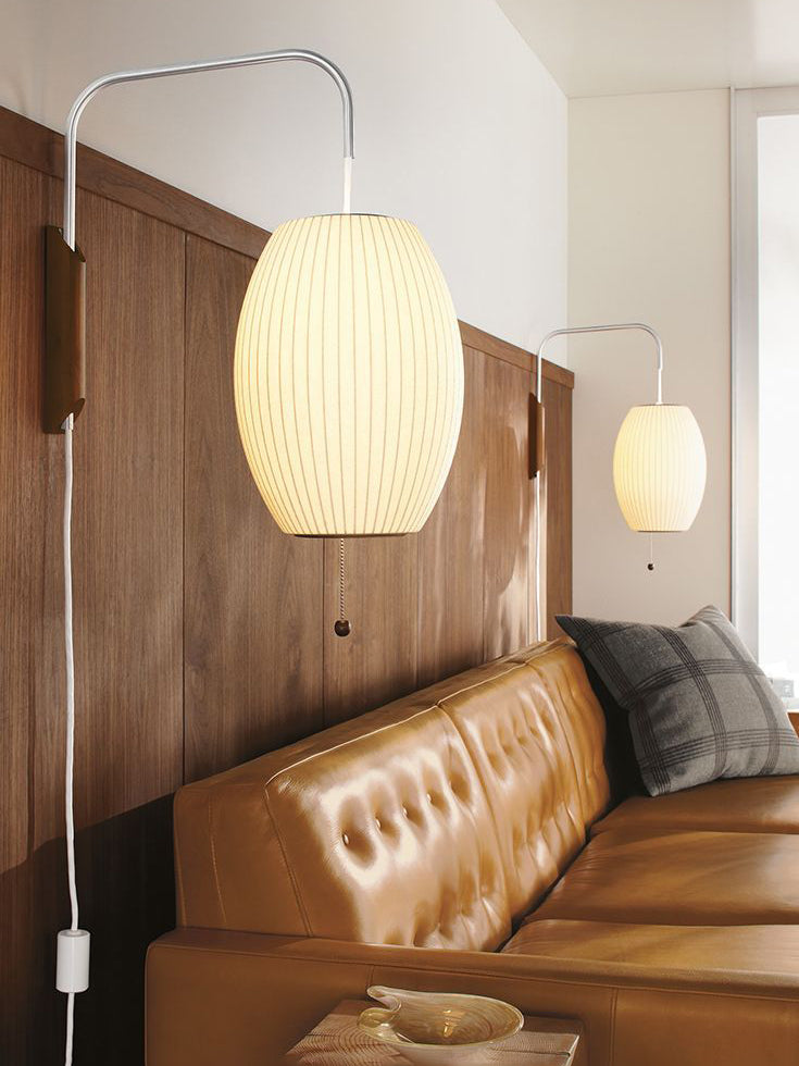 A lit oval Clérachic wall light on a walnut wall panel above a tan leather sofa, with a second lit shade further along.