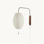Oval ribbed shade and curved steel arm of this Clérachic wall light on a soft cream backdrop, with a walnut bracket and bead pull.