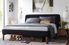 Two oval Clérachic wall lights on either side of a black upholstered bed with grey bedding, above walnut bedside tables.