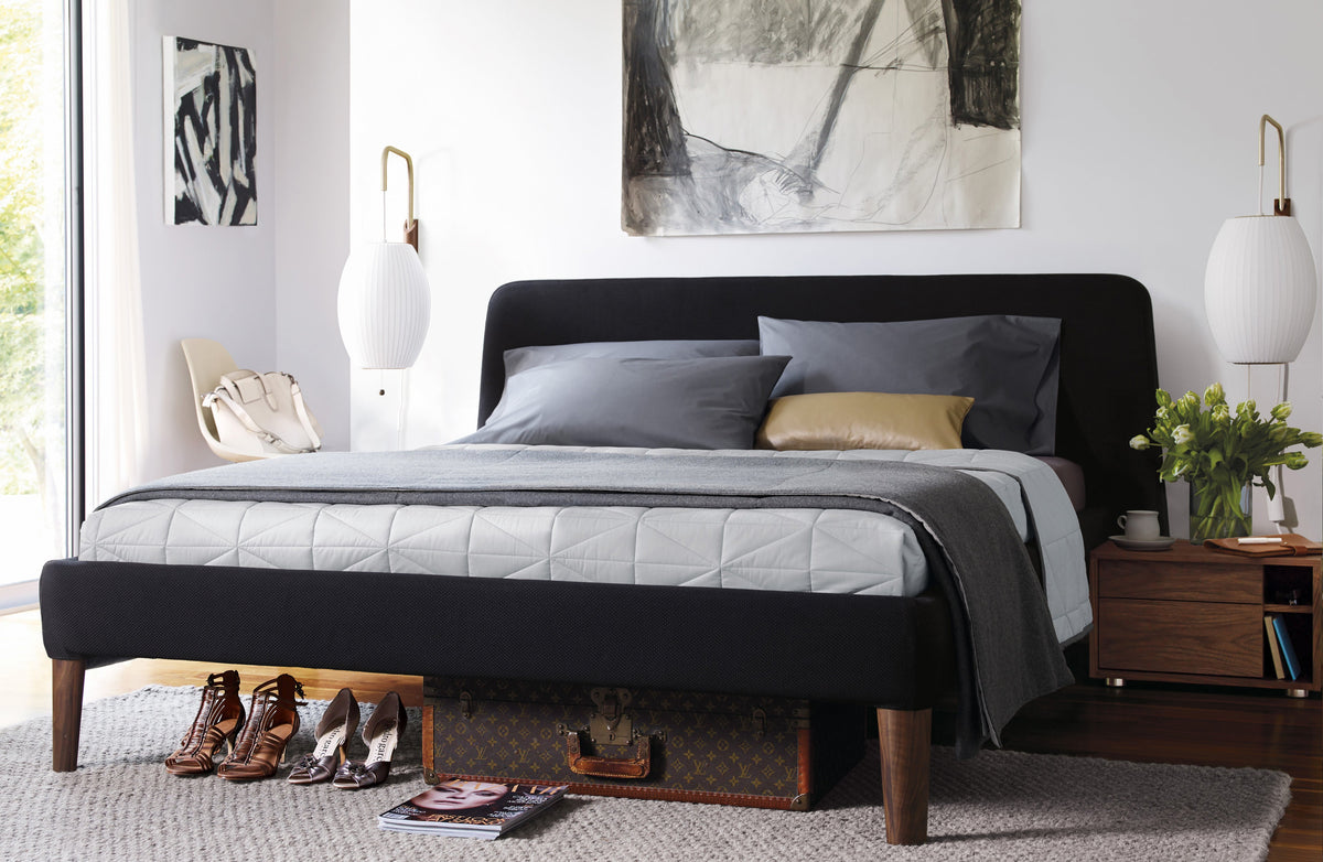 Two oval Clérachic wall lights on either side of a black upholstered bed with grey bedding, above walnut bedside tables.