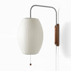 Large view of the oval shade, steel arm and walnut bracket of this Clérachic wall light on a bright white backdrop.