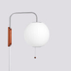 Round white shade on a steel arm, with the walnut bracket and bead pull of this Clérachic wall light, on a soft grey backdrop.