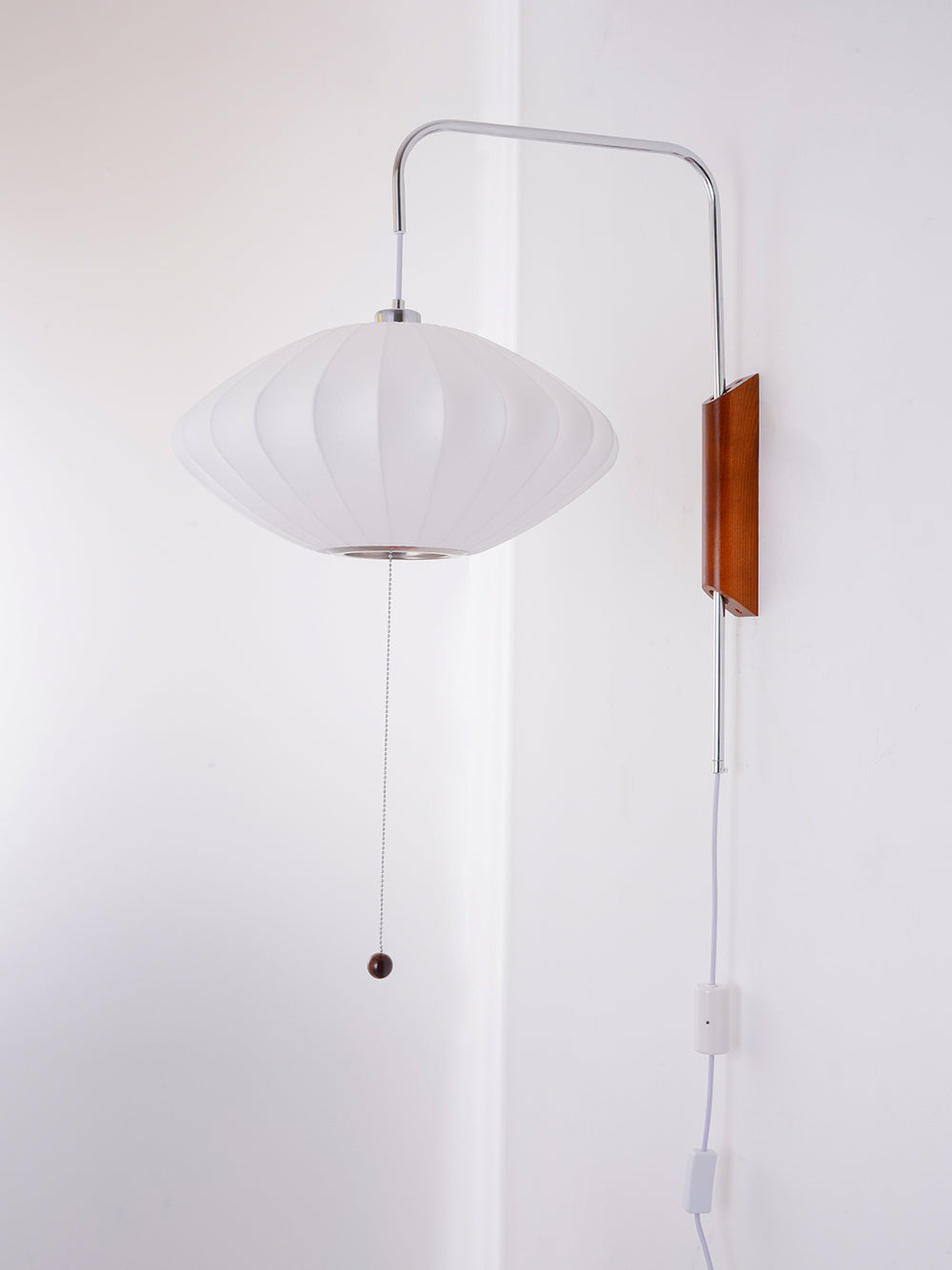 Unlit saucer-shaped shade on this Clérachic wall light, with its pull cord, white cable and in-line switch against a pale wall corner.