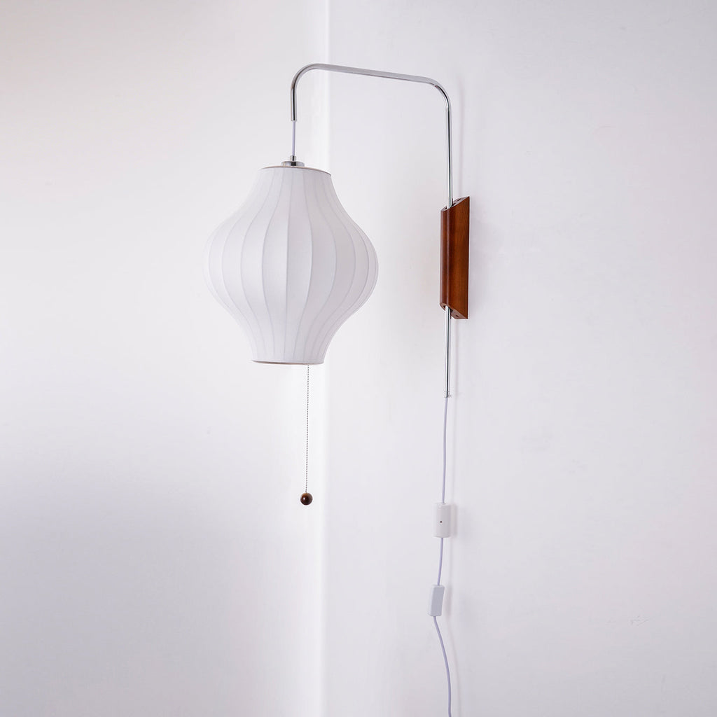 A pear-shaped white shade hangs from a Clérachic wall light on a curved arm, with its pull cord and in-line switch beside a wall corner.