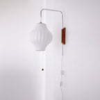 A pear-shaped white shade hangs from a Clérachic wall light on a curved arm, with its pull cord and in-line switch beside a wall corner.