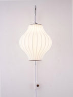 Lit pear-shaped shade on a Clérachic wall light glowing evenly, with its wooden bead pull and in-line switch at the lower edge.