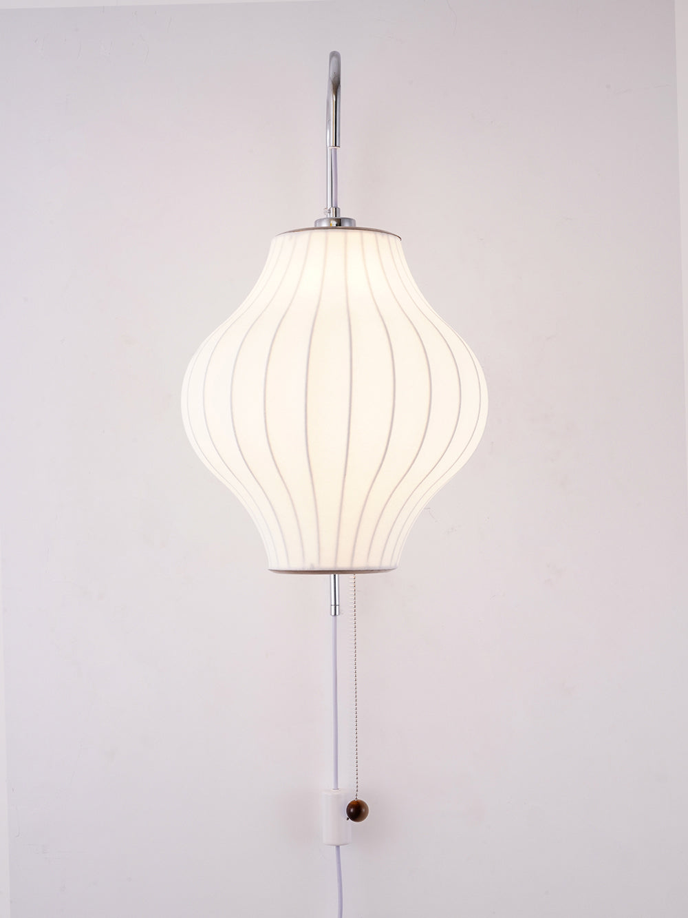 Lit pear-shaped shade on a Clérachic wall light glowing evenly, with its wooden bead pull and in-line switch at the lower edge.