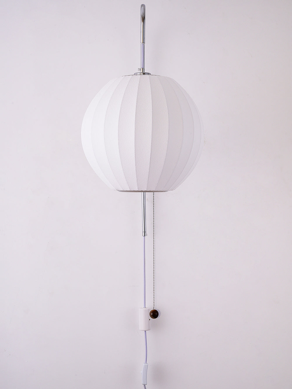 Round white shade of a Clérachic wall light, unlit, with its cable and wooden bead running down a pale wall.
