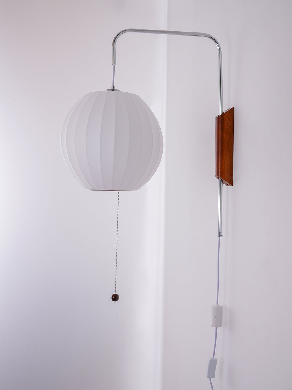 An unlit round shade on a Clérachic wall light, with a walnut bracket, steel arm and pull cord on a lilac-tinged wall.