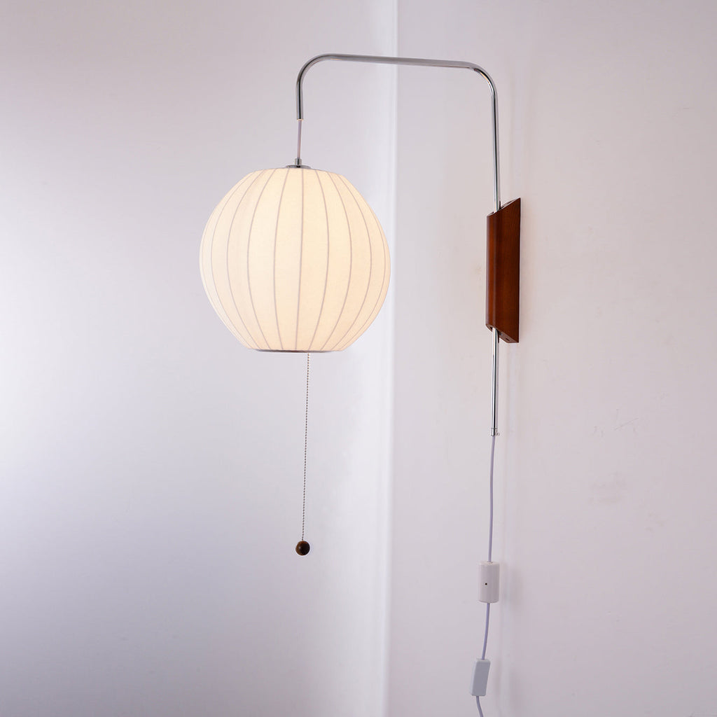 Lit round shade glowing a warm cream on this Clérachic wall light, with its pull cord and in-line switch on a pale wall.