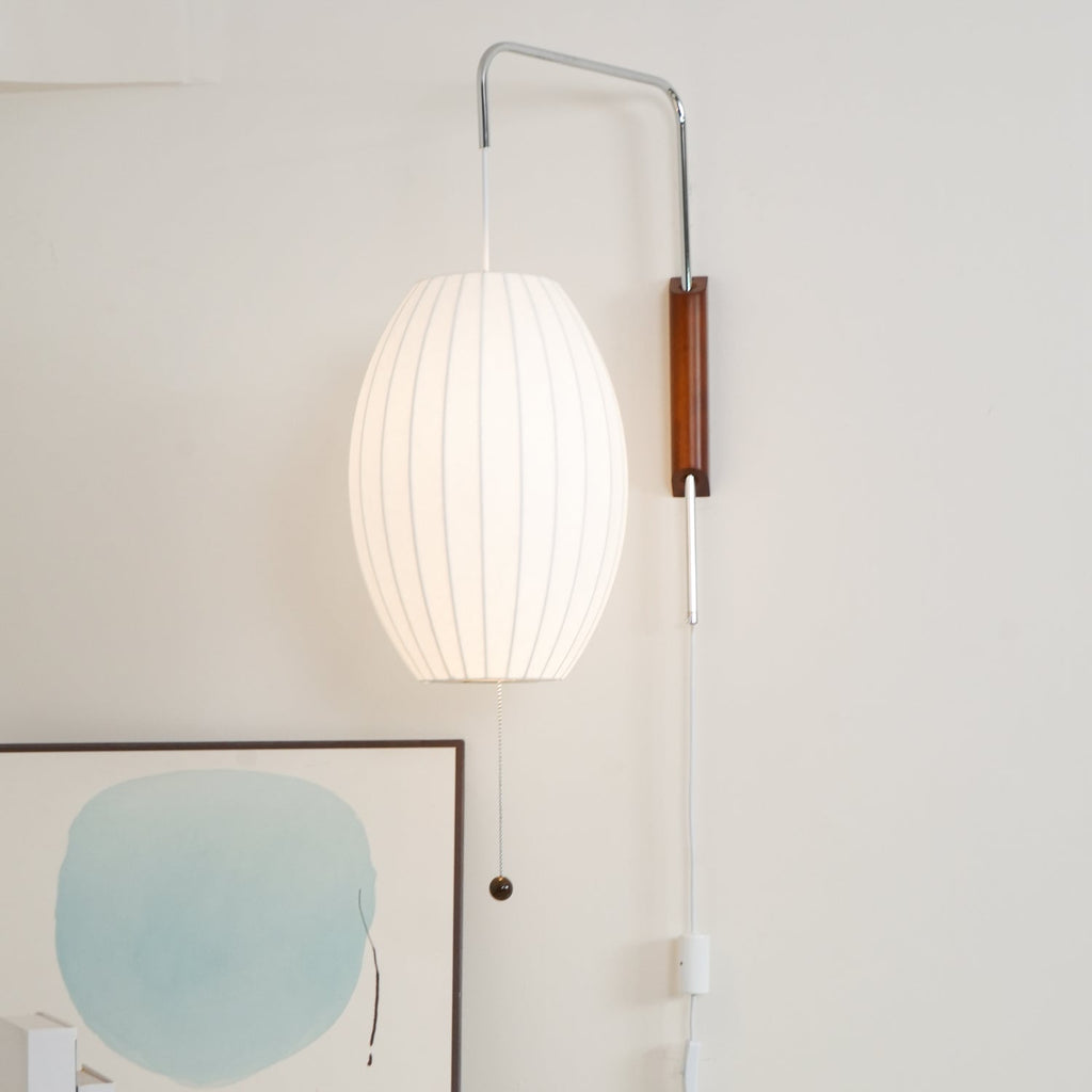 Lit oval shade on a Clérachic wall light above an in-line switch, with a pale blue abstract artwork propped below.