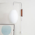 Unlit oval shade of a Clérachic wall light in bright white, with a walnut bracket and a framed blue artwork below.