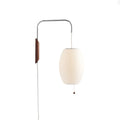 Warm-white oval shade on a Clérachic wall light with a walnut bracket, bead pull and long white cable, on a plain white backdrop.