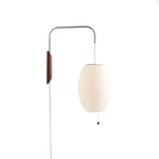 Warm-white oval shade on a Clérachic wall light with a walnut bracket, bead pull and long white cable, on a plain white backdrop.