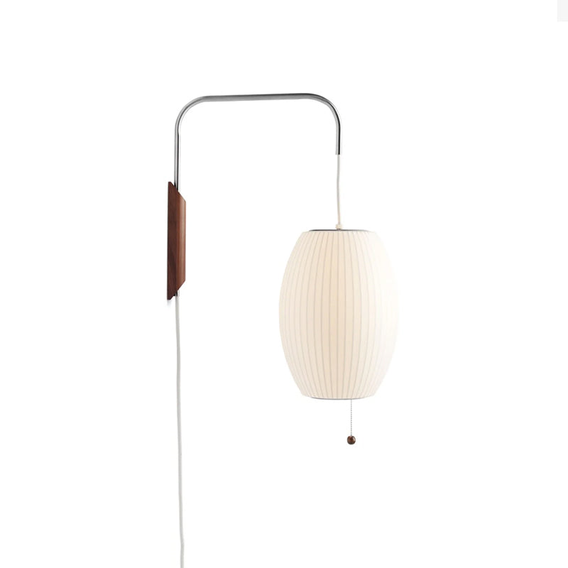 Warm-white oval shade on a Clérachic wall light with a walnut bracket, bead pull and long white cable, on a plain white backdrop.