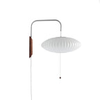 A flat saucer-shaped white shade hangs from a Clérachic wall arm with a walnut bracket and bead pull on a plain white backdrop.
