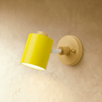 Clérachic wall lamp with a bright yellow cylindrical metal shade and white arm on a pale wood backplate, on a limewash wall.