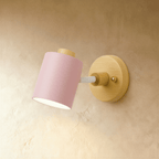 Clérachic wall lamp with a soft pink cylindrical metal shade and white arm on a light wooden backplate, on a limewash wall.