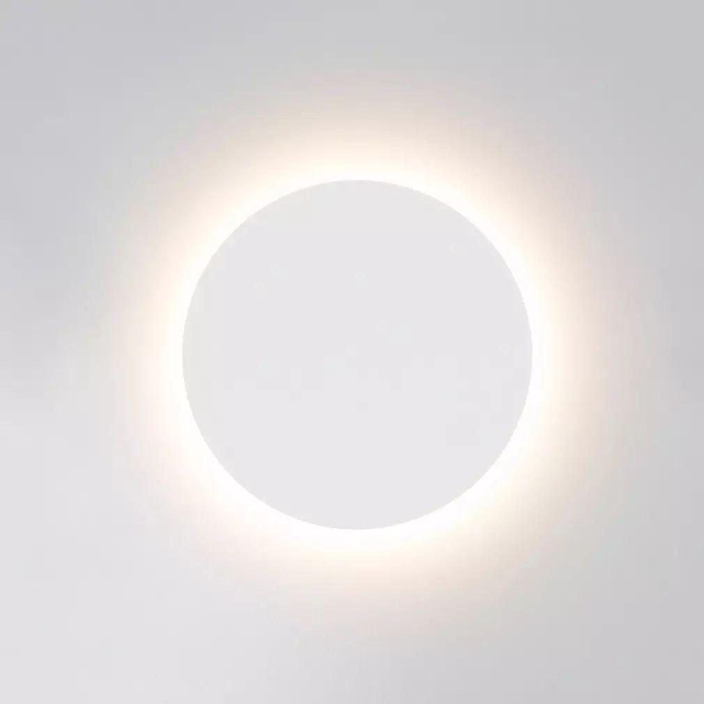 White round Clérachic wall light switched on, a bright ring of light spreading around the disk onto a pale wall.