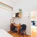 White round Clérachic wall light above a small wooden desk with a wall shelf, a black chair and a framed print.