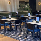 A pair of brass Clérachic disk lights on a green panelled wall above booth seating and blue chairs in a restaurant.