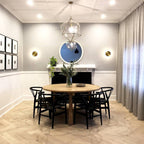 Two brass Clérachic disk lights flank a round mirror and fireplace in a dining room with a round wooden table.