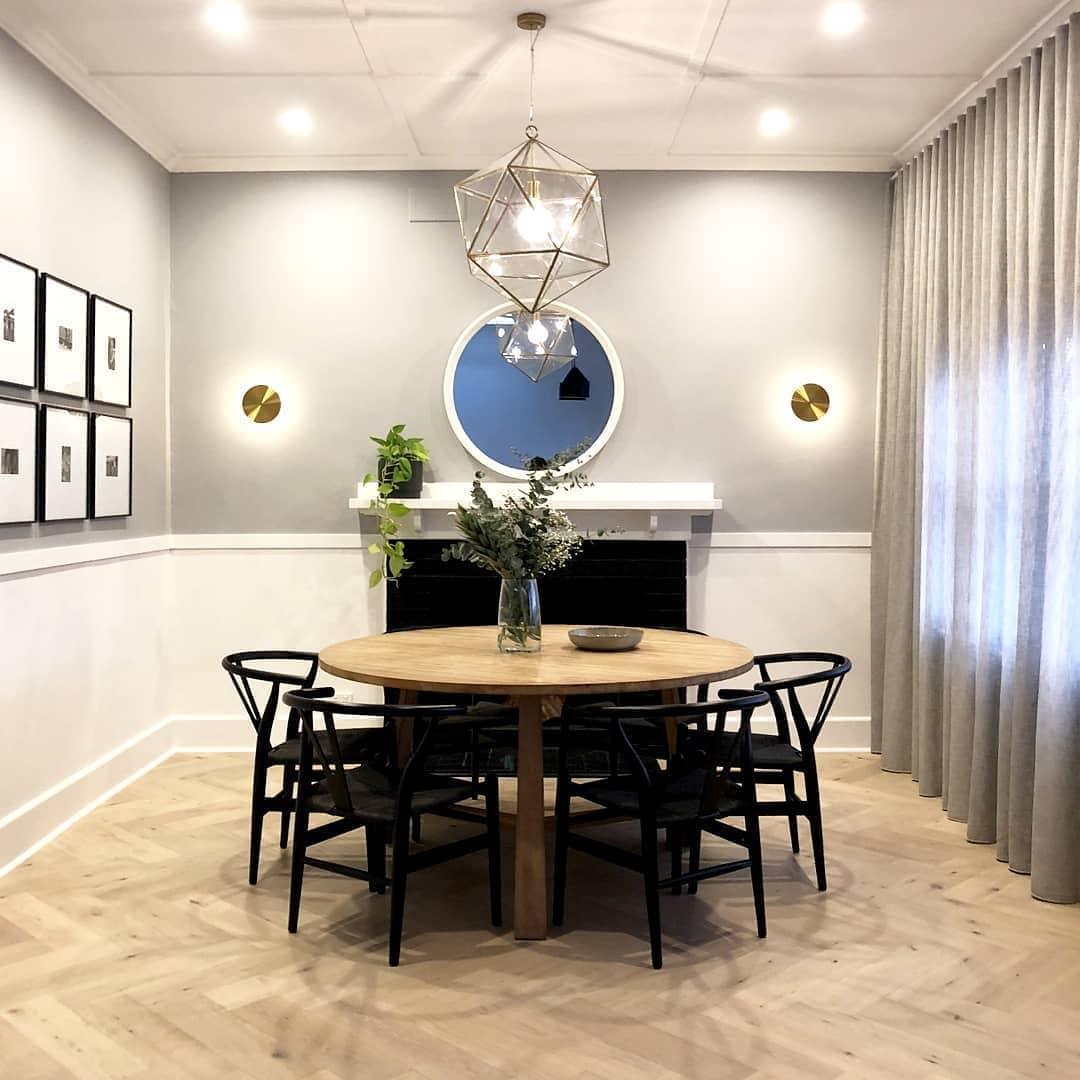 Two brass Clérachic disk lights flank a round mirror and fireplace in a dining room with a round wooden table.