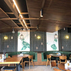 Small brass Clérachic disk lights on a dark green bamboo-style wall in a restaurant with wooden ceiling slats and green booths.
