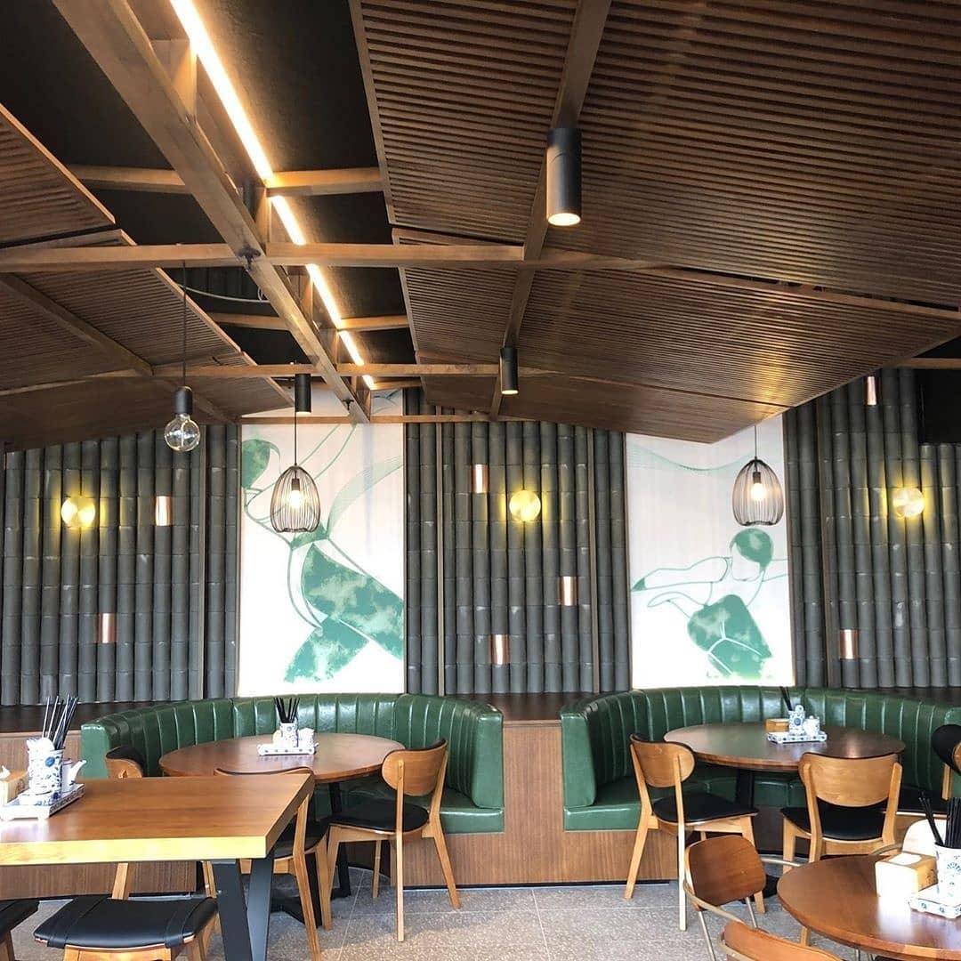 Small brass Clérachic disk lights on a dark green bamboo-style wall in a restaurant with wooden ceiling slats and green booths.