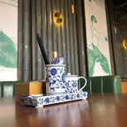 A brass Clérachic disk light lit on a green tube-clad wall above a table with a blue and white teapot and chopsticks.