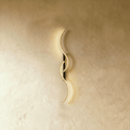 Clérachic S-shaped wall light with two interlocking gold LED curves on a slim black backplate, glowing against warm limewashed plaster.