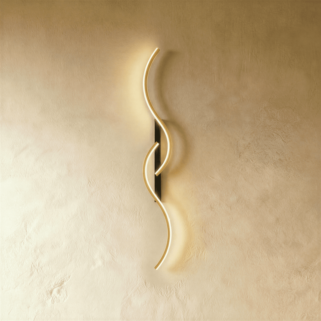 Clérachic tall S-shaped wall light with two overlapping gold LED curves on a slim black backplate, lit against warm plaster.