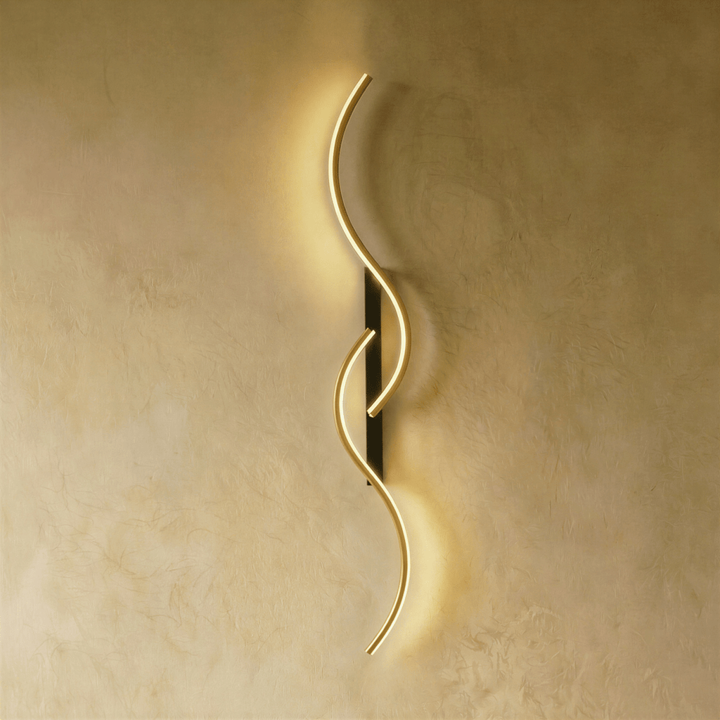 Clérachic S-shaped wall light with two linked gold-toned LED curves and a narrow black backplate, giving a warm glow on plaster.