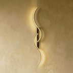 Clérachic S-shaped wall light with two linked gold-toned LED curves and a narrow black backplate, giving a warm glow on plaster.