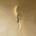 Clérachic black S-shaped wall light with two interlocking LED curves, glowing warm white against a golden limewashed wall.