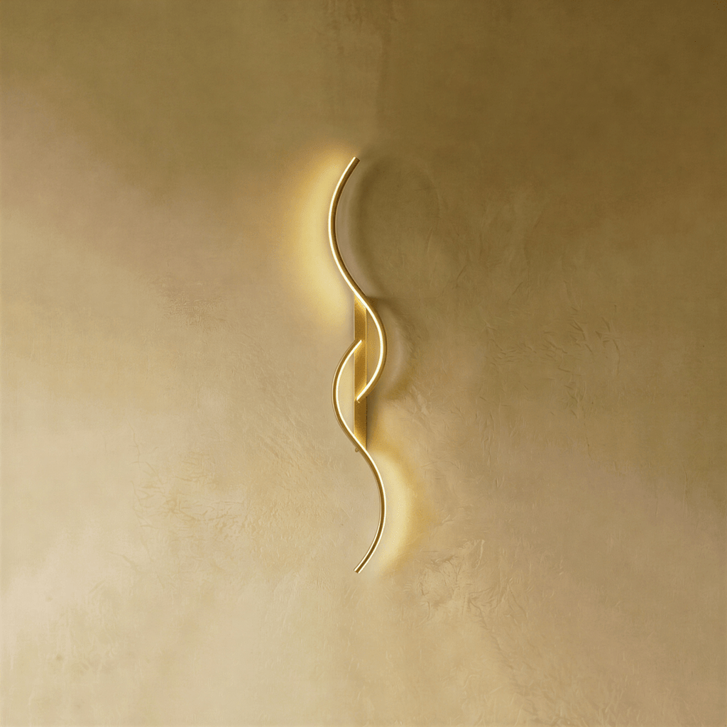 Clérachic gold S-shaped wall light with two interlocking LED curves and a matching gold backplate, glowing on warm plaster.