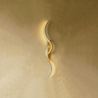 Clérachic gold S-shaped wall light with two interlocking LED curves and a matching gold backplate, glowing on warm plaster.
