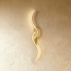 Clérachic gold S-shaped wall light, curves and slim backplate in one brushed gold finish, lit softly against pale plaster.