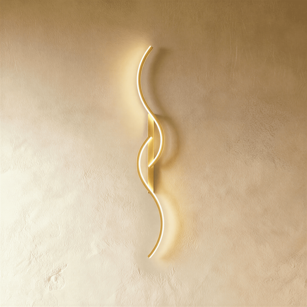 Clérachic gold S-shaped wall light, curves and slim backplate in one brushed gold finish, lit softly against pale plaster.