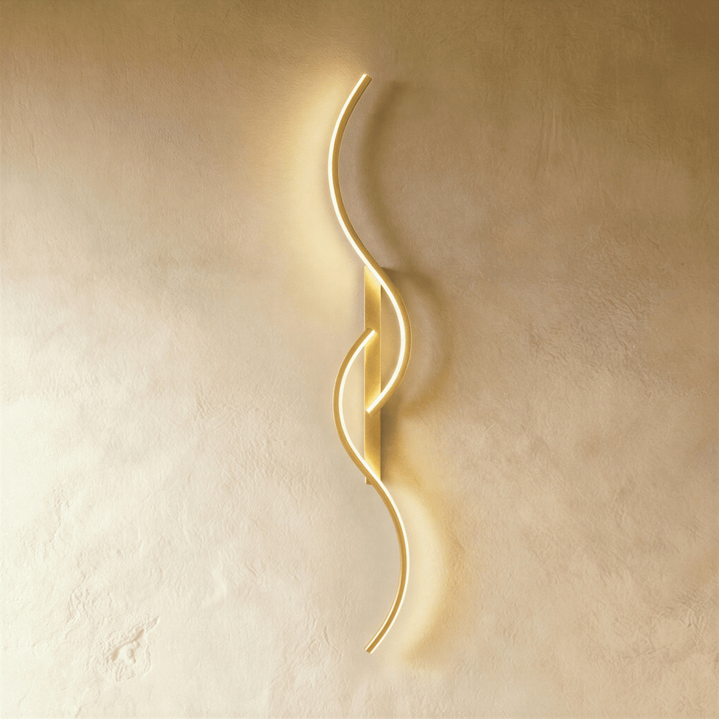 Clérachic tall gold S-shaped wall light with two overlapping LED curves on a gold backplate, glowing against pale plaster.