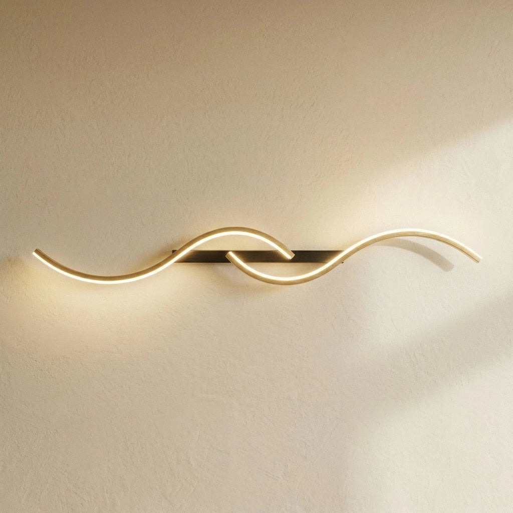 Clérachic S-shaped wall light turned horizontal, with gold LED curves on a black bar, glowing against a sunlit plaster wall.