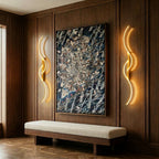 Clérachic pair of gold S-shaped wall lights flanking a large framed painting on walnut panelling above a cream bench.