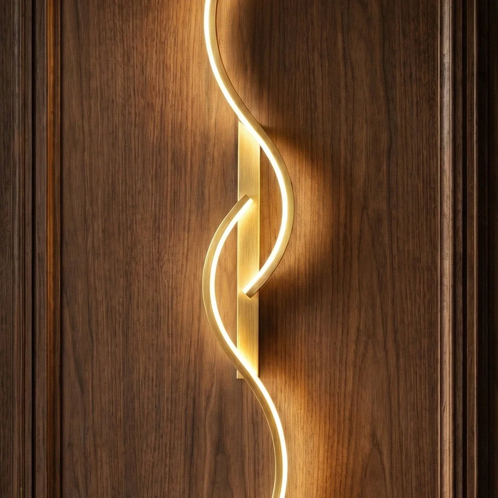Close view of a Clérachic gold S-shaped wall light, showing the brushed gold backplate and glowing LED curve on walnut panelling.