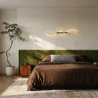 Clérachic black S-shaped wall light mounted horizontally above a green velvet headboard in a bedroom with a brown linen bed.