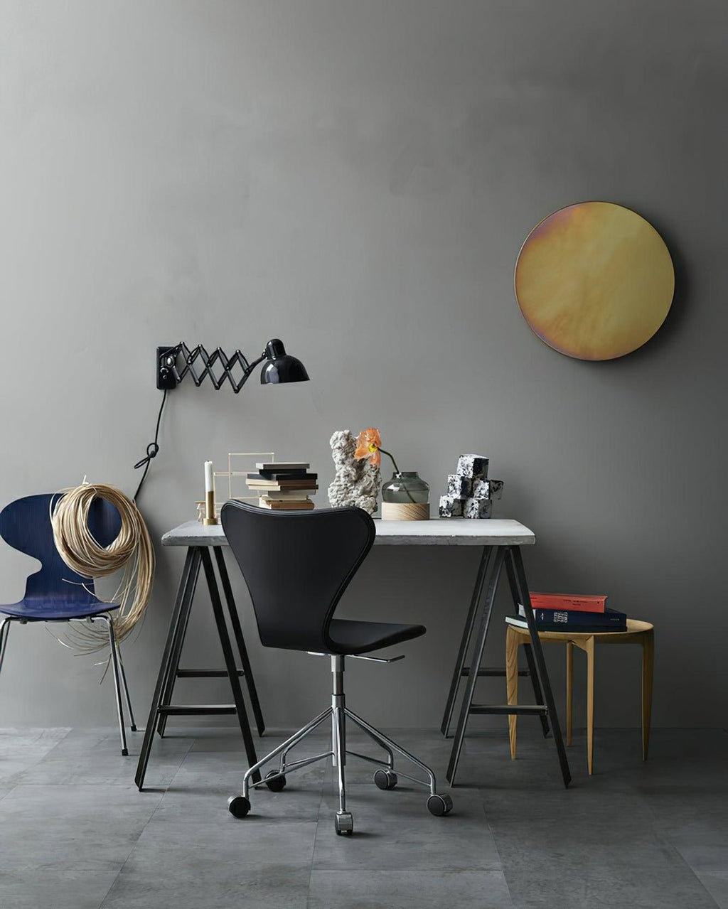 Black Clérachic scissor-arm wall light above a small desk with a black swivel chair, against a grey wall.