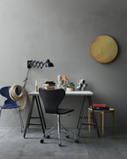 Black Clérachic scissor-arm wall light above a small desk with a black swivel chair, against a grey wall.