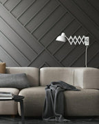 White Clérachic scissor-arm wall light on a dark panelled wall above a beige sofa with a grey throw.
