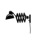 Glossy black Clérachic scissor-arm wall light with its arm angled out, the shade shining, on a white backdrop.