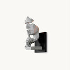 This Clérachic wall light on a plain backdrop: a white sculpted face with a finger to its lips, mounted on a black square plate.