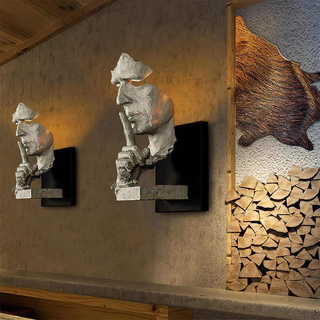 Two white Clérachic face wall lights glowing on a rough plaster wall, beside a stack of split logs and a fur hide.